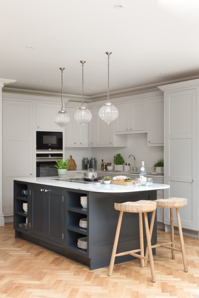 Design ideas for a mid-sized traditional l-shaped open plan kitchen in Surrey with an undermount sink, shaker cabinets, blue cabinets, quartzite benchtops, white splashback, panelled appliances, light hardwood floors, with island, brown floor and white benchtop.