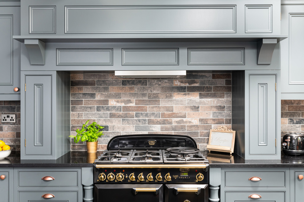 Photo of a mid-sized traditional l-shaped eat-in kitchen in Dorset with beaded inset cabinets, grey cabinets, quartzite benchtops, stone tile splashback, with island and black benchtop.