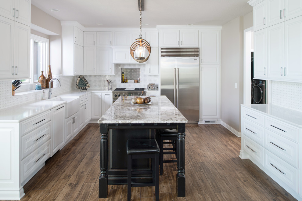 Design ideas for a transitional u-shaped open plan kitchen in Kansas City with a farmhouse sink, raised-panel cabinets, white cabinets, quartz benchtops, white splashback, mosaic tile splashback, stainless steel appliances, porcelain floors, with island, brown floor and white benchtop.