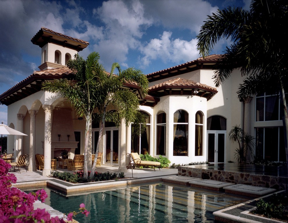 Photo of a mid-sized mediterranean backyard custom-shaped lap pool in Miami with a hot tub and natural stone pavers.