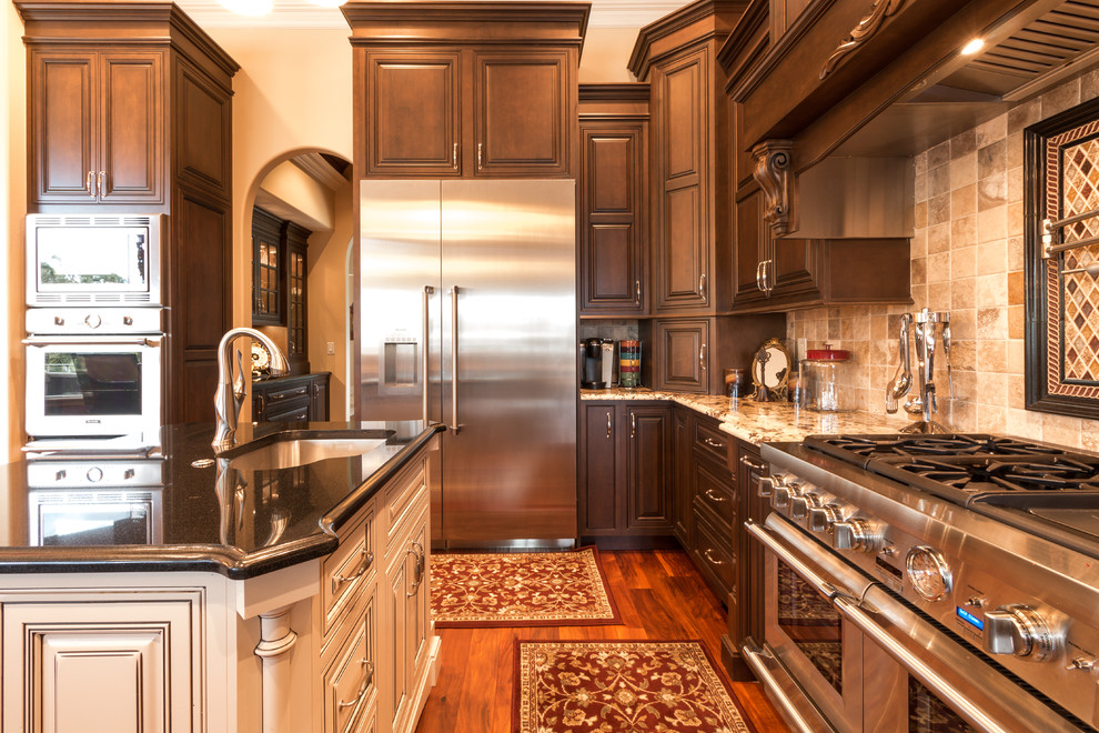 Mid-sized traditional open plan kitchen in Orlando with raised-panel cabinets, dark wood cabinets, with island, an undermount sink, granite benchtops, brown splashback, stone tile splashback, stainless steel appliances, medium hardwood floors and brown floor.