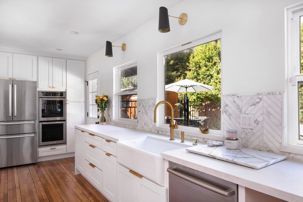 Mid-sized transitional galley medium tone wood floor and brown floor eat-in kitchen photo in Los Angeles with a farmhouse sink, shaker cabinets, white cabinets, quartz countertops, multicolored backsplash, marble backsplash, stainless steel appliances, no island and gray countertops