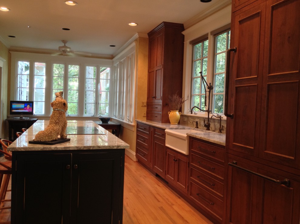 This is an example of a small traditional single-wall open plan kitchen in Charleston with a farmhouse sink, beaded inset cabinets, medium wood cabinets, marble benchtops, stone slab splashback, panelled appliances, light hardwood floors and with island.