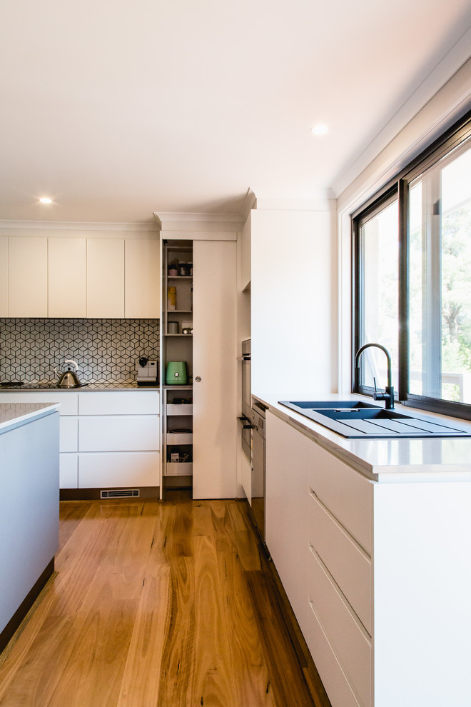 This is an example of a contemporary l-shaped kitchen in Canberra - Queanbeyan with a double-bowl sink, white cabinets, mosaic tile splashback, stainless steel appliances, white splashback and with island.