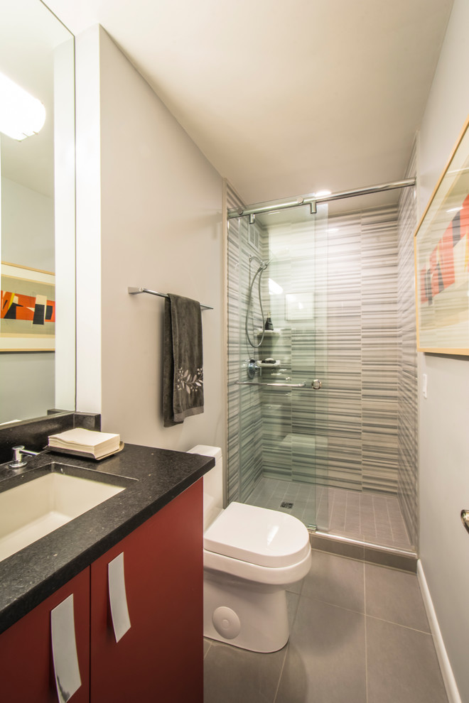 Inspiration for a small modern bathroom in Baltimore with flat-panel cabinets, red cabinets, an alcove shower, a two-piece toilet, gray tile, ceramic tile, white walls, ceramic floors, an undermount sink, granite benchtops, grey floor, a sliding shower screen and black benchtops.