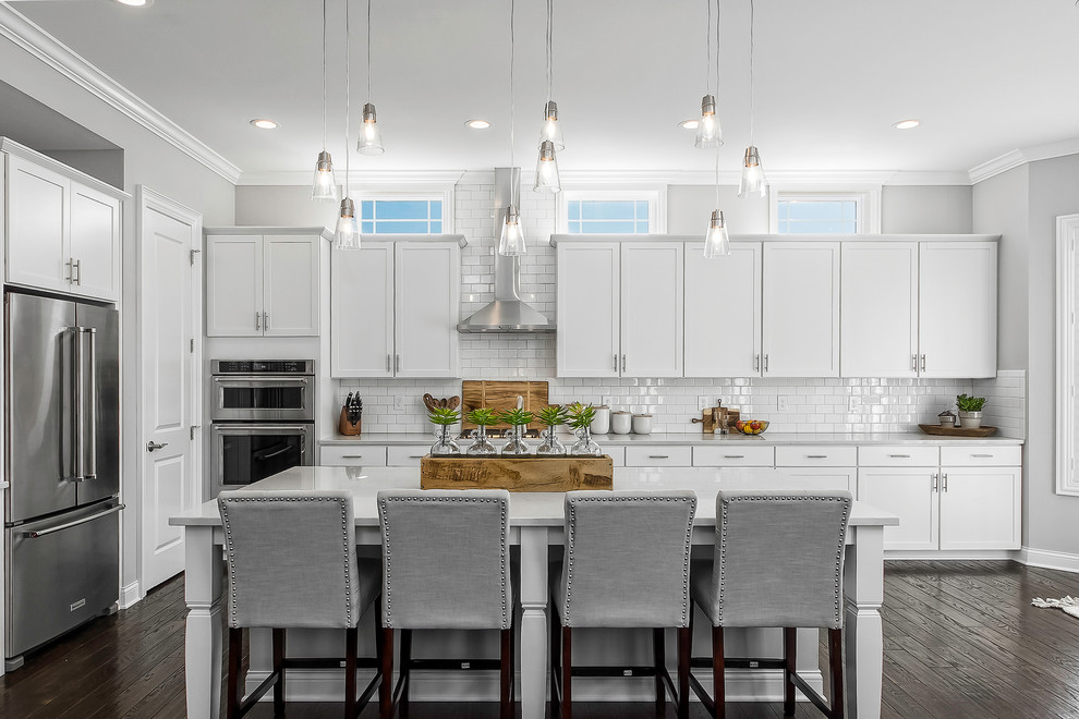Inspiration for a transitional kitchen in Columbus with shaker cabinets, white cabinets, white splashback, subway tile splashback, stainless steel appliances, dark hardwood floors, with island, brown floor and grey benchtop.