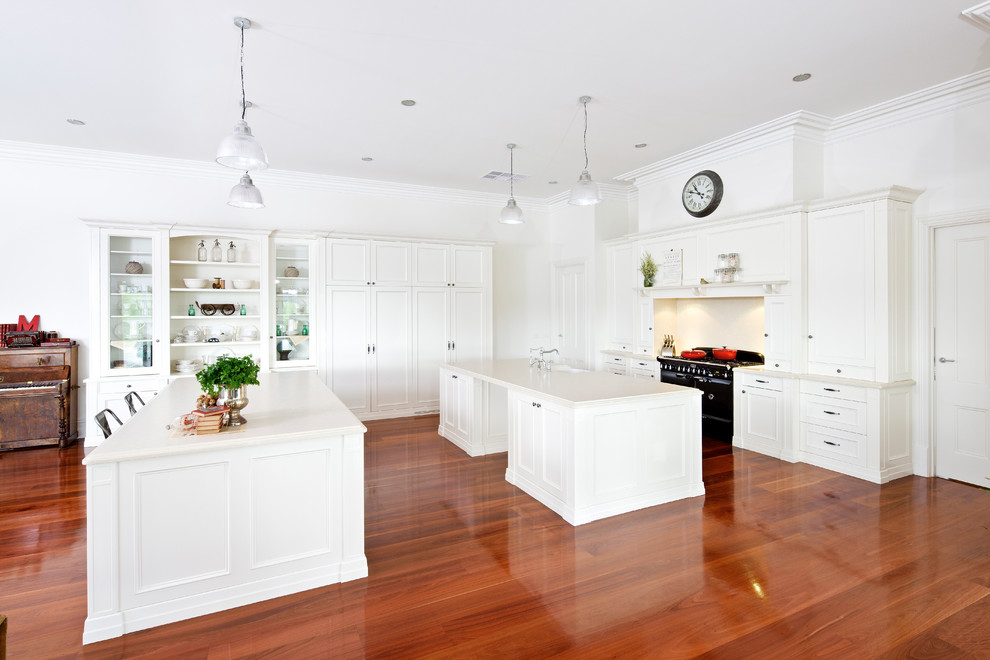 This is an example of a transitional eat-in kitchen in Melbourne with a farmhouse sink, shaker cabinets, white cabinets, black appliances, medium hardwood floors and multiple islands.