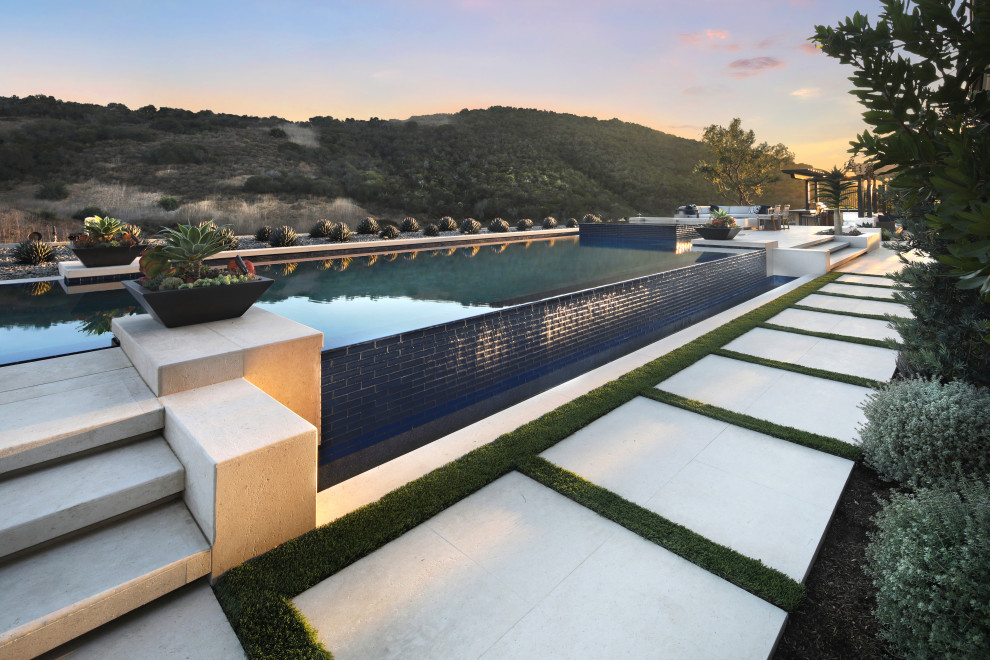 Imagen de piscina infinita grande rectangular en patio trasero con paisajismo de piscina y adoquines de piedra natural