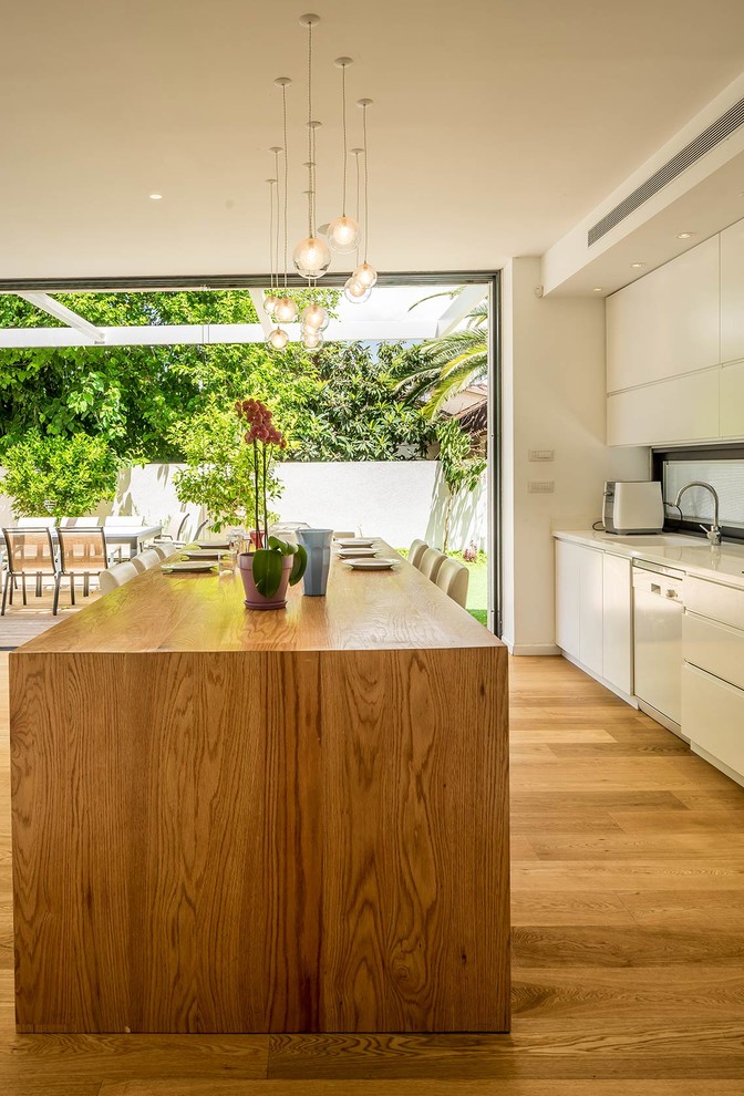 Small modern galley open plan kitchen in Tel Aviv with a drop-in sink, flat-panel cabinets, white cabinets, wood benchtops, stainless steel appliances, light hardwood floors and with island.