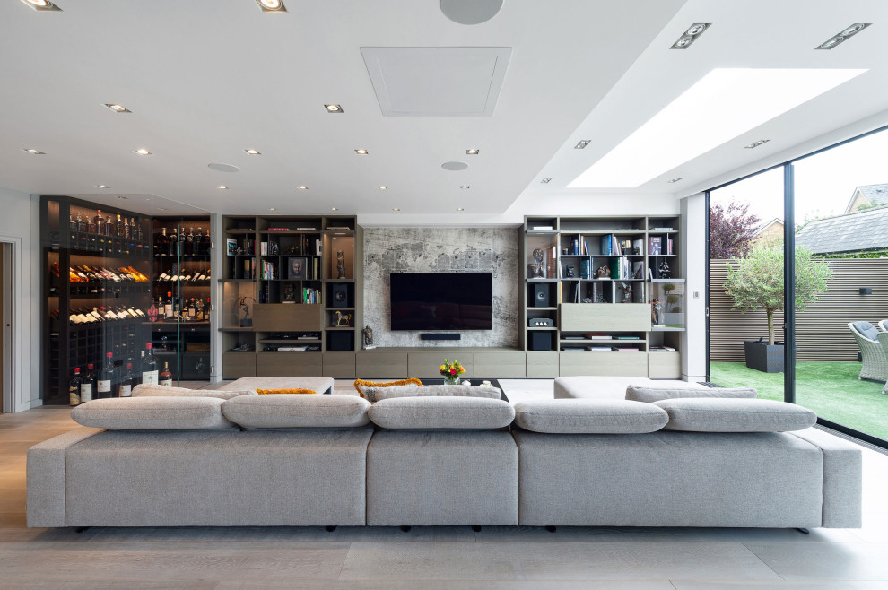 This is an example of an expansive contemporary open concept family room in London with light hardwood floors, no fireplace, a wall-mounted tv, beige floor and a library.
