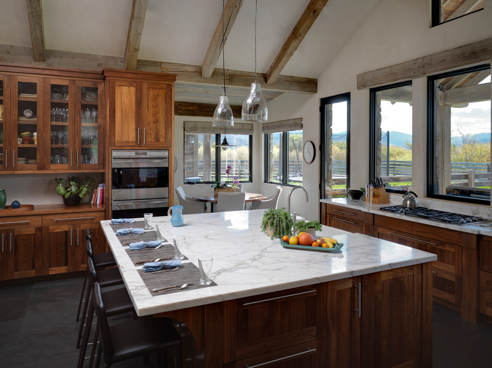 Eat-in kitchen - large rustic u-shaped eat-in kitchen idea with a farmhouse sink, shaker cabinets, medium tone wood cabinets, stainless steel appliances, an island, marble countertops, white backsplash and stone slab backsplash
