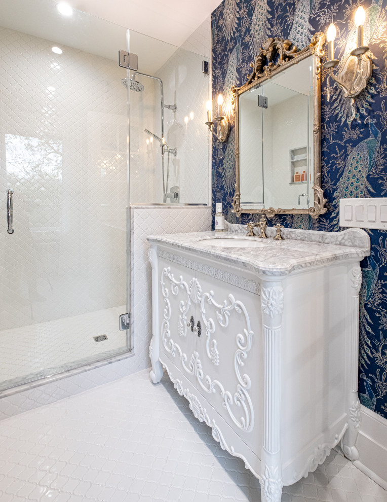 Photo of a mid-sized eclectic master bathroom in Newark with furniture-like cabinets, white cabinets, an alcove shower, a one-piece toilet, white tile, cement tile, blue walls, ceramic floors, an undermount sink, marble benchtops, white floor, a hinged shower door, grey benchtops, a single vanity, a freestanding vanity and wallpaper.