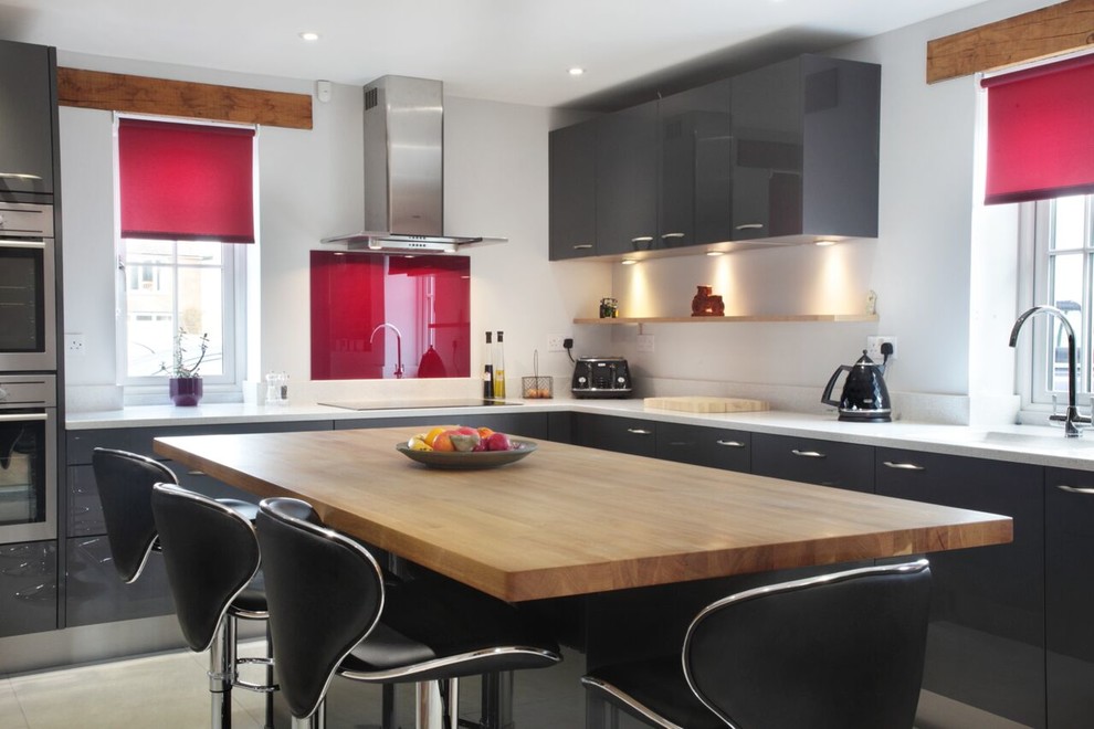 Photo of a large contemporary l-shaped eat-in kitchen in Buckinghamshire with flat-panel cabinets, grey cabinets, red splashback, glass sheet splashback, stainless steel appliances, with island, an integrated sink, wood benchtops and porcelain floors.