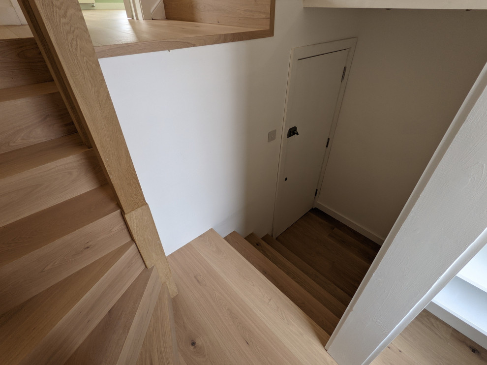 This is an example of a small modern wood curved staircase in London with wood risers and wood railing.
