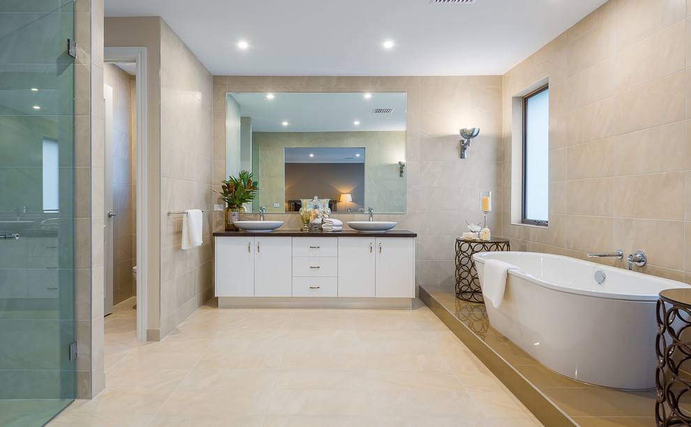 This is an example of a contemporary bathroom in Melbourne with a freestanding tub, a curbless shower, beige tile, beige walls and a vessel sink.