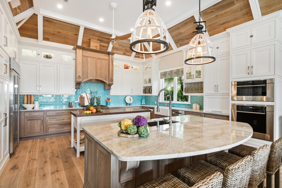 Inspiration for a large tropical u-shaped open plan kitchen in Other with an undermount sink, beaded inset cabinets, white cabinets, quartzite benchtops, blue splashback, glass tile splashback, stainless steel appliances, light hardwood floors, multiple islands, brown floor, beige benchtop and wood.
