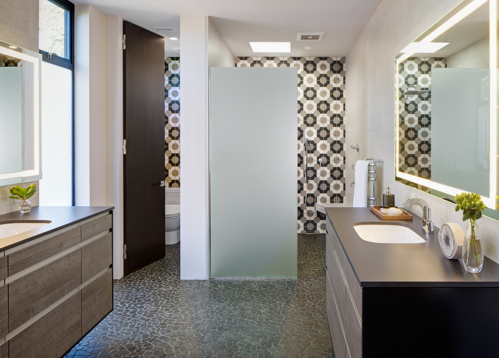 This is an example of a mid-sized modern master bathroom in San Diego with flat-panel cabinets, distressed cabinets, an alcove shower, a one-piece toilet, beige tile, black tile, white tile, porcelain tile, white walls, pebble tile floors, an undermount sink, solid surface benchtops, grey floor and an open shower.
