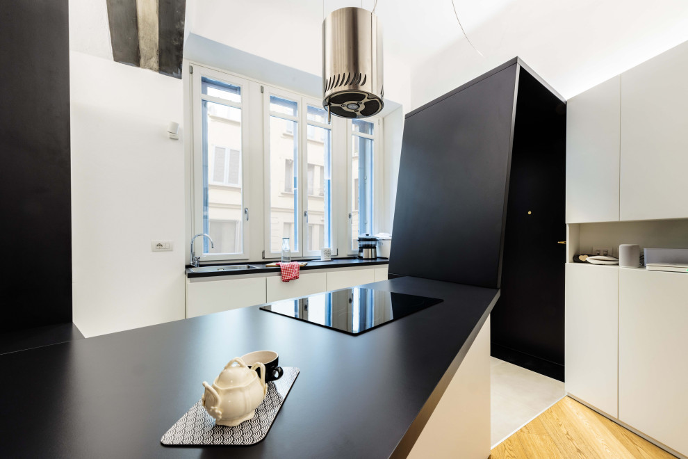 Small contemporary l-shaped eat-in kitchen in Milan with an undermount sink, flat-panel cabinets, white cabinets, laminate benchtops, window splashback, stainless steel appliances, ceramic floors, a peninsula, beige floor and black benchtop.
