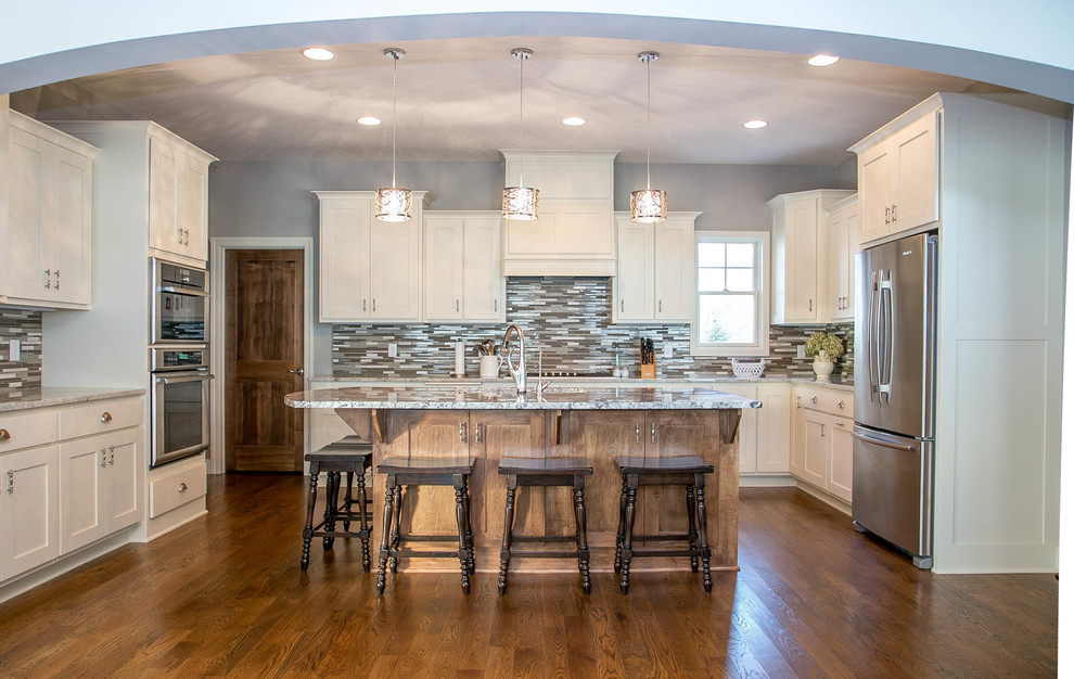 Inspiration for a transitional u-shaped medium tone wood floor open concept kitchen remodel in Minneapolis with an undermount sink, shaker cabinets, white cabinets, granite countertops, multicolored backsplash, ceramic backsplash, stainless steel appliances and an island