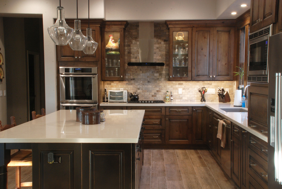 Example of a mid-sized mountain style l-shaped porcelain tile eat-in kitchen design in Phoenix with an undermount sink, raised-panel cabinets, quartzite countertops, mosaic tile backsplash, stainless steel appliances, an island, dark wood cabinets and beige backsplash