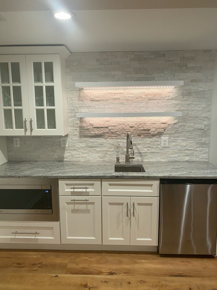 Transitional single-wall wet bar in Other with an undermount sink, recessed-panel cabinets, white cabinets, granite benchtops, white splashback, stone tile splashback and vinyl floors.