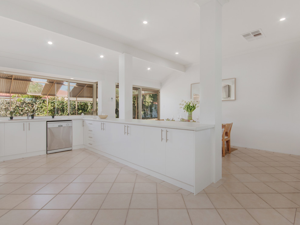 Large beach style u-shaped open plan kitchen with a double-bowl sink, flat-panel cabinets, white cabinets, laminate benchtops, white splashback, subway tile splashback, stainless steel appliances, ceramic floors, with island and beige floor.