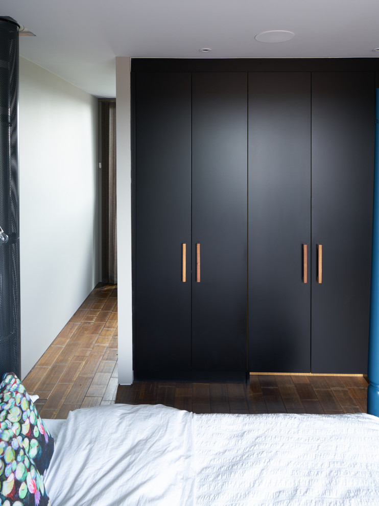 Large contemporary gender-neutral built-in wardrobe in London with bamboo floors, flat-panel cabinets and black cabinets.