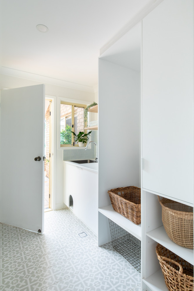 Photo of a medium sized nautical single-wall separated utility room in Brisbane with flat-panel cabinets, white walls, porcelain flooring, grey floors, white cabinets, blue splashback, porcelain splashback, a built-in sink, laminate countertops, a stacked washer and dryer and white worktops.