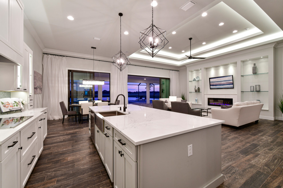 Example of a mid-sized transitional l-shaped porcelain tile and brown floor eat-in kitchen design with a farmhouse sink, shaker cabinets, white cabinets, quartz countertops, metallic backsplash, glass tile backsplash, stainless steel appliances, an island and white countertops