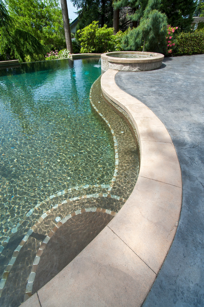 Design ideas for a mediterranean backyard custom-shaped infinity pool in Vancouver with a hot tub and stamped concrete.