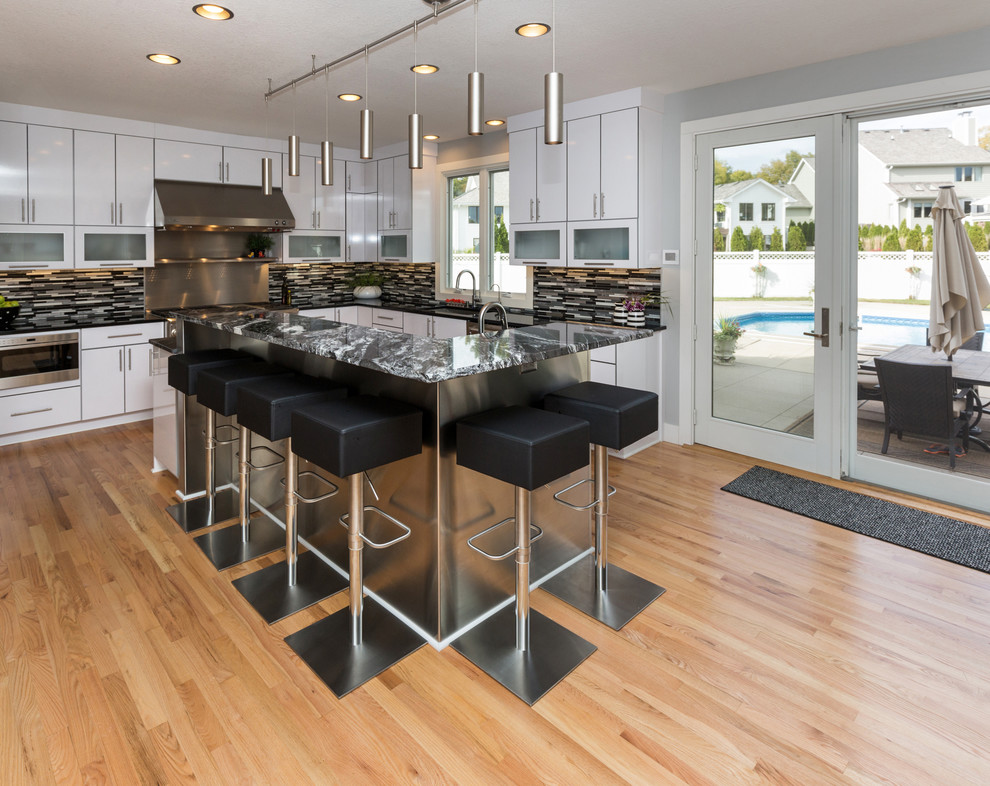Inspiration for a large contemporary u-shaped light wood floor open concept kitchen remodel with an undermount sink, flat-panel cabinets, white cabinets, granite countertops, multicolored backsplash, mosaic tile backsplash, stainless steel appliances and an island
