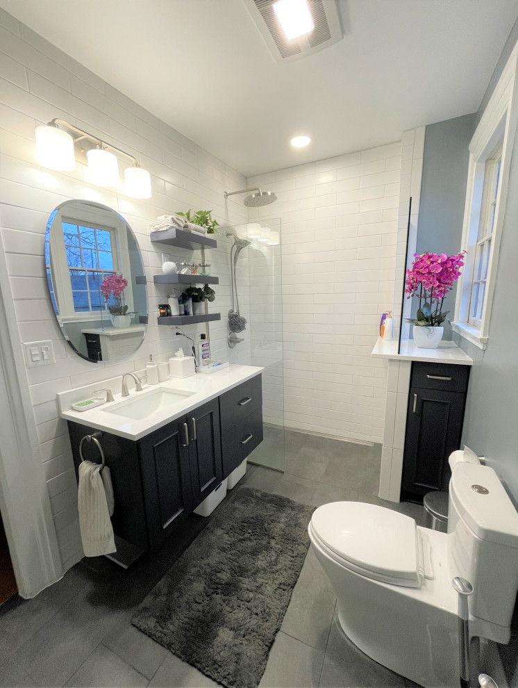 This is an example of a mid-sized transitional master bathroom in Detroit with recessed-panel cabinets, blue cabinets, a curbless shower, a two-piece toilet, white tile, ceramic tile, blue walls, porcelain floors, an undermount sink, engineered quartz benchtops, grey floor, an open shower, white benchtops, a single vanity and a floating vanity.