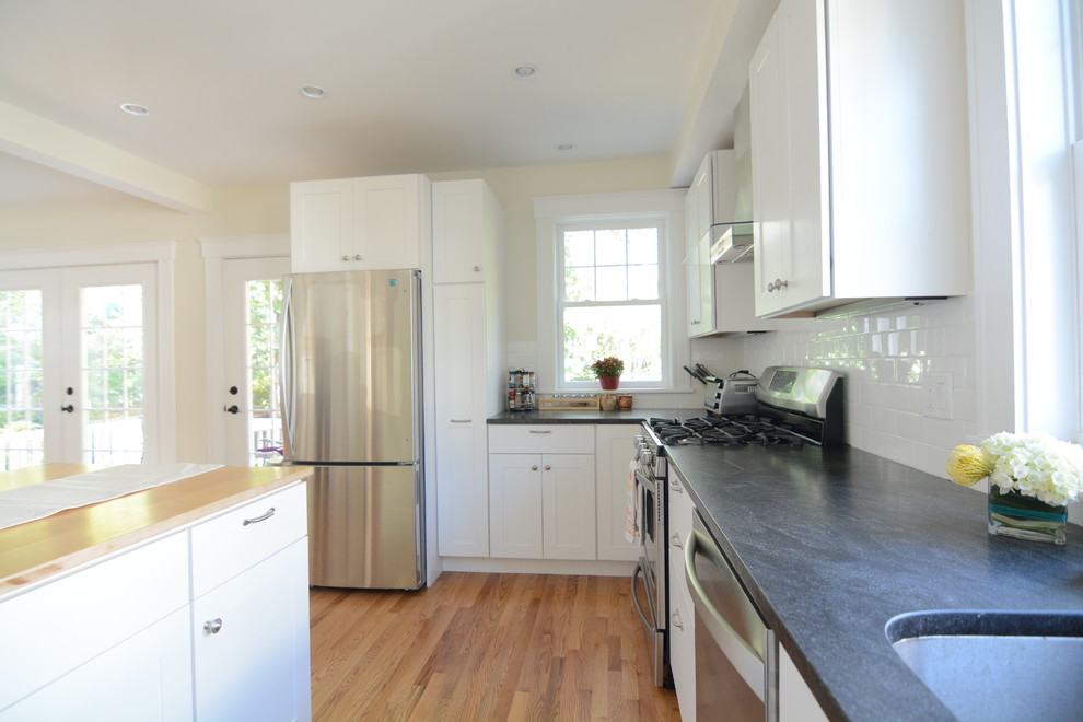 Kitchen pantry - large transitional l-shaped medium tone wood floor and brown floor kitchen pantry idea in Boston with a drop-in sink, flat-panel cabinets, white cabinets, solid surface countertops, white backsplash, subway tile backsplash, stainless steel appliances and an island