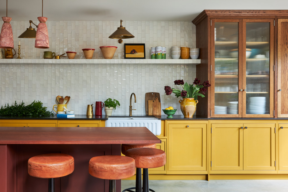 Offene, Einzeilige, Mittelgroße Klassische Küche mit Landhausspüle, Schrankfronten im Shaker-Stil, gelben Schränken, Mineralwerkstoff-Arbeitsplatte, Küchenrückwand in Weiß, Rückwand aus Keramikfliesen, Kücheninsel und schwarzer Arbeitsplatte in London