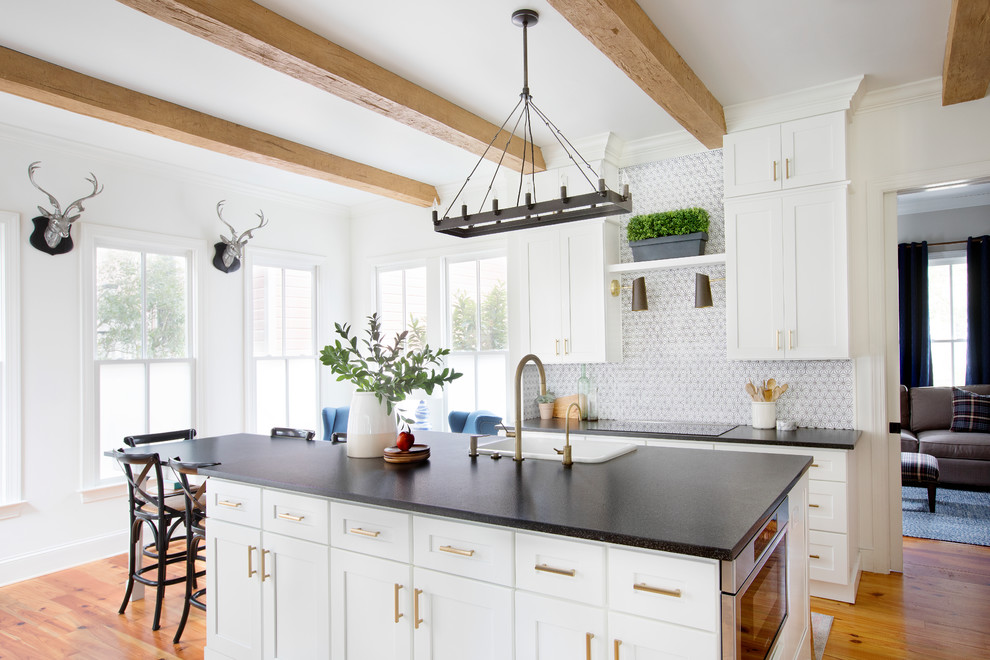 This is an example of a mid-sized beach style separate kitchen in Charleston with a drop-in sink, shaker cabinets, white cabinets, multi-coloured splashback, stainless steel appliances, medium hardwood floors, with island, black benchtop, quartz benchtops, ceramic splashback and brown floor.