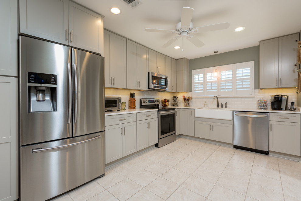 Enclosed kitchen - large transitional l-shaped enclosed kitchen idea with a farmhouse sink, shaker cabinets, gray cabinets, quartzite countertops, white backsplash, subway tile backsplash, stainless steel appliances and no island