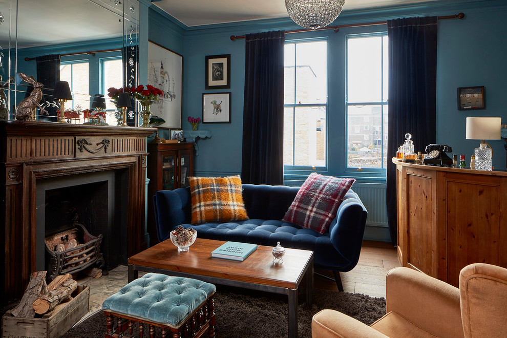 Inspiration for an eclectic enclosed family room in London with a home bar, blue walls, medium hardwood floors, a standard fireplace, a metal fireplace surround and brown floor.