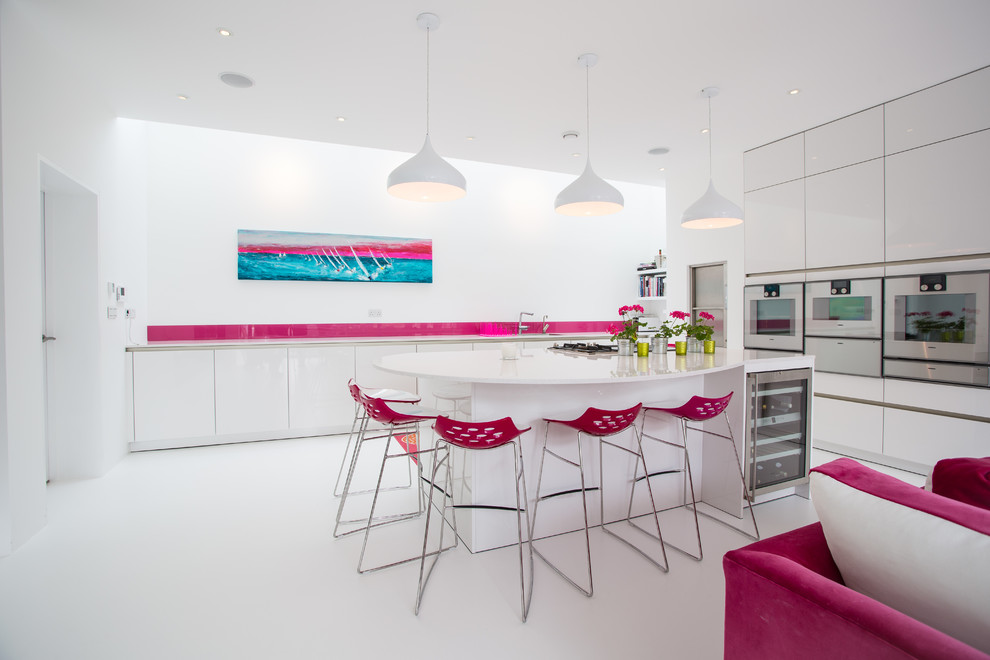 This is an example of a large contemporary u-shaped open plan kitchen in Hampshire with an undermount sink, flat-panel cabinets, white cabinets, solid surface benchtops, pink splashback, glass sheet splashback, stainless steel appliances and with island.