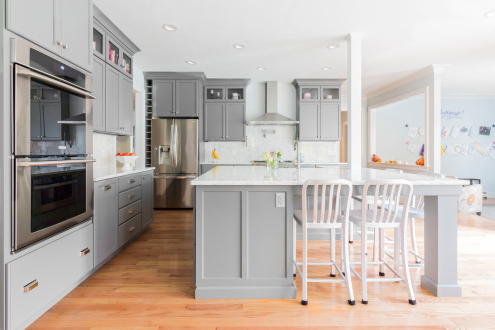 Design ideas for a mid-sized transitional l-shaped kitchen in Boston with recessed-panel cabinets, grey cabinets, white splashback, stainless steel appliances, medium hardwood floors, with island, quartz benchtops and stone slab splashback.