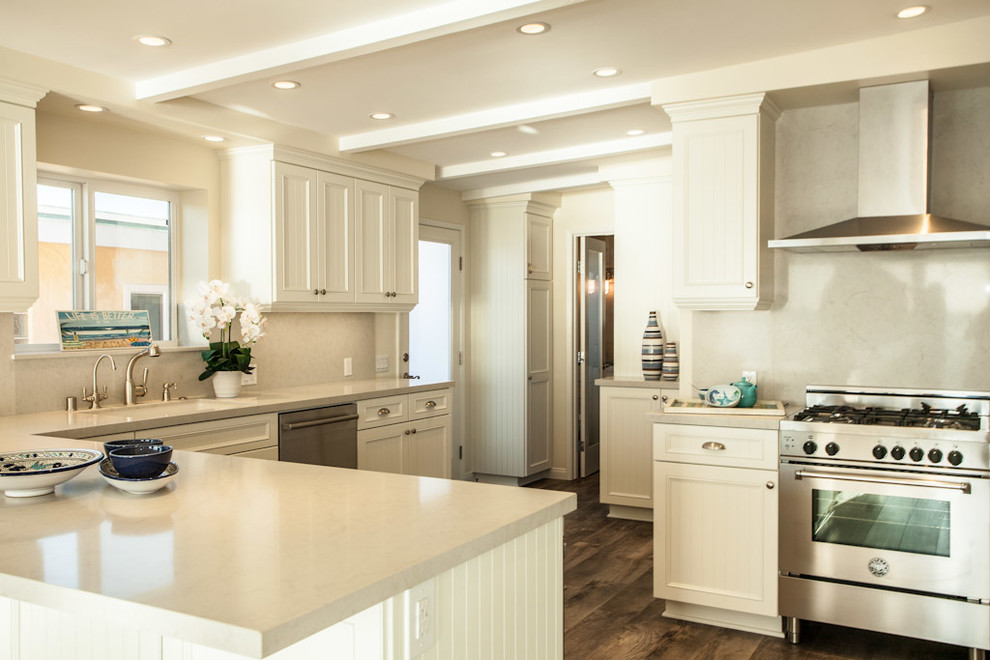 This is an example of a mid-sized beach style l-shaped open plan kitchen in San Diego with an undermount sink, white cabinets, quartzite benchtops, white splashback, stainless steel appliances, louvered cabinets, stone slab splashback, medium hardwood floors and a peninsula.