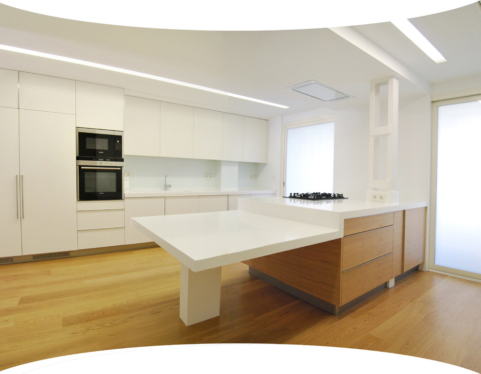 Photo of a large modern single-wall separate kitchen in Valencia with an integrated sink, flat-panel cabinets, white cabinets, quartz benchtops, white splashback, window splashback, stainless steel appliances, laminate floors, with island and brown floor.