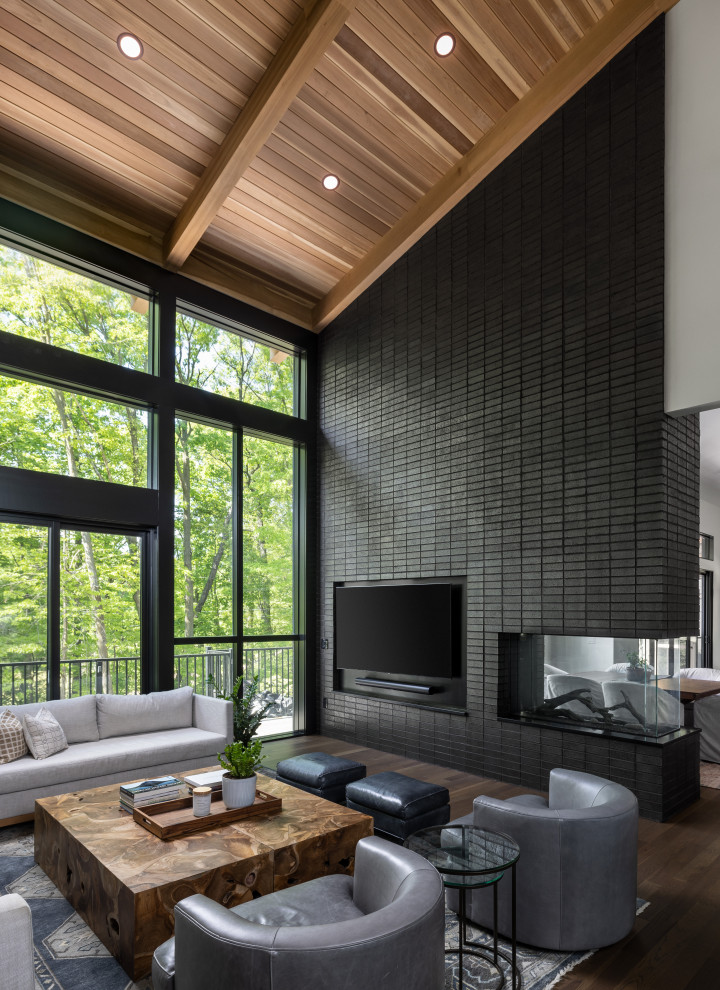 This is an example of an expansive transitional formal living room in Detroit with white walls, dark hardwood floors, a two-sided fireplace, a brick fireplace surround, brown floor and wood.