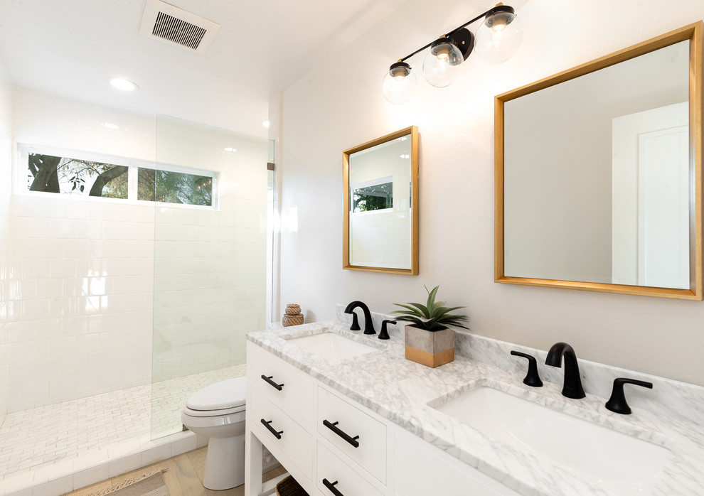 Photo of a large beach style kids bathroom in Santa Barbara with shaker cabinets, black cabinets, an alcove tub, a shower/bathtub combo, a two-piece toilet, white tile, ceramic tile, white walls, light hardwood floors, a drop-in sink, marble benchtops, a shower curtain and white benchtops.