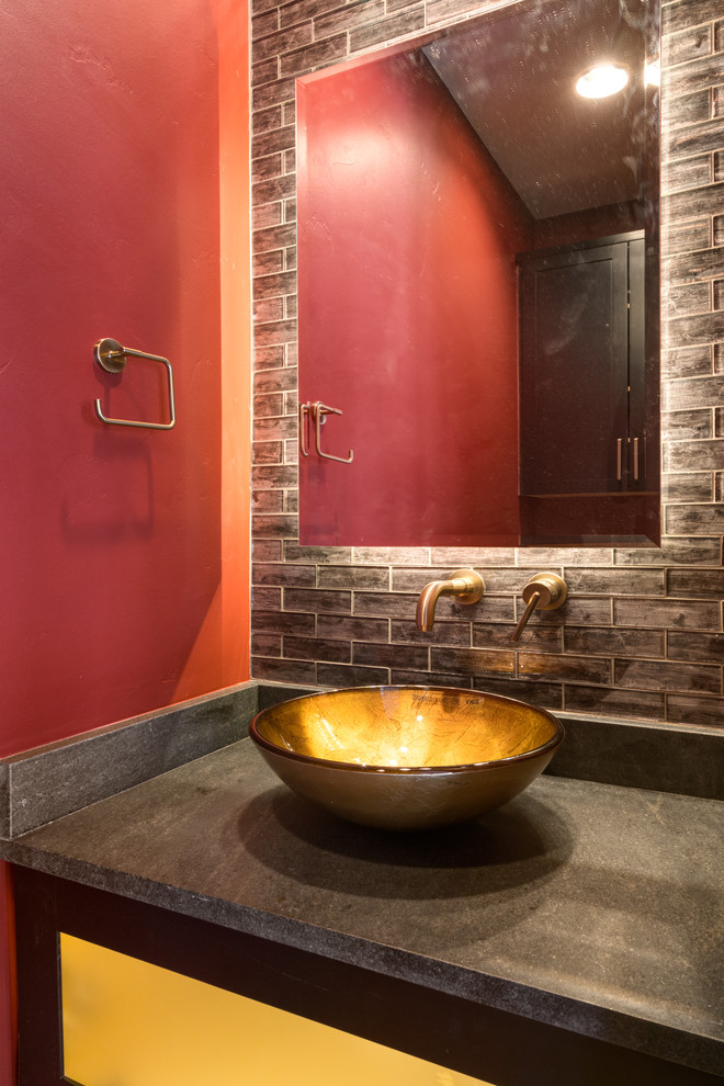 This is an example of a small contemporary powder room in Denver with recessed-panel cabinets, dark wood cabinets, brown tile, glass tile, red walls, medium hardwood floors, a vessel sink, soapstone benchtops, brown floor and black benchtops.