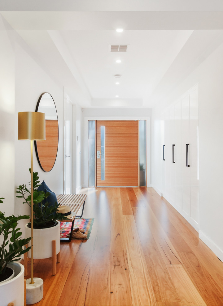 Inspiration for a contemporary foyer in Melbourne with white walls, medium hardwood floors, a single front door, a medium wood front door and brown floor.