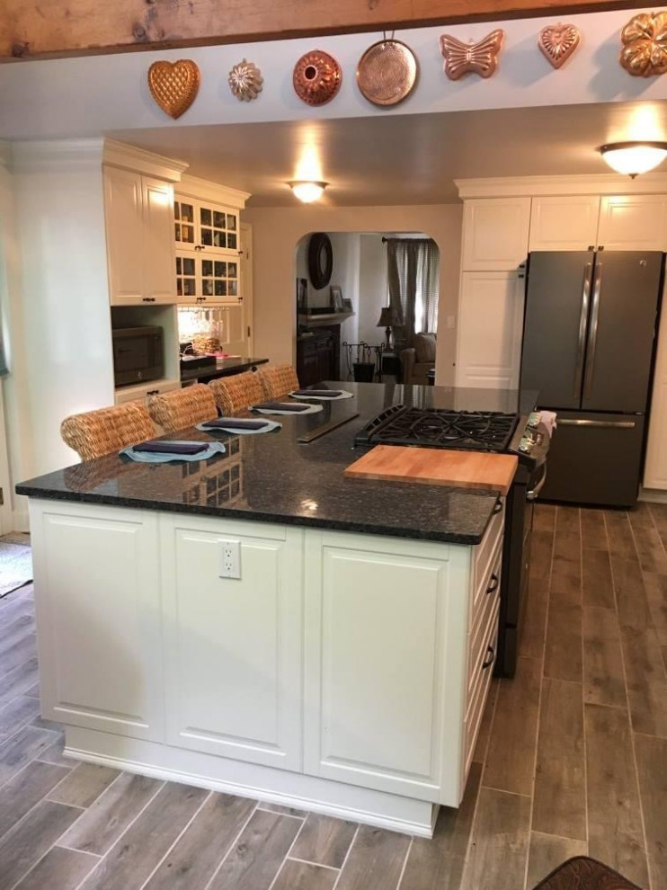 This is an example of a large beach style eat-in kitchen in Los Angeles with an undermount sink, raised-panel cabinets, white cabinets, granite benchtops, blue splashback, mosaic tile splashback, stainless steel appliances, ceramic floors, with island, grey floor, blue benchtop and vaulted.