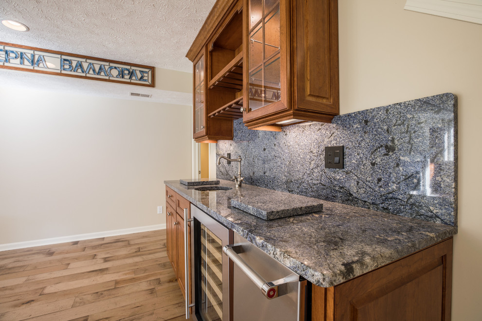 This is an example of a mid-sized transitional single-wall wet bar in Detroit with an undermount sink, shaker cabinets, medium wood cabinets, granite benchtops, blue splashback, light hardwood floors and blue benchtop.