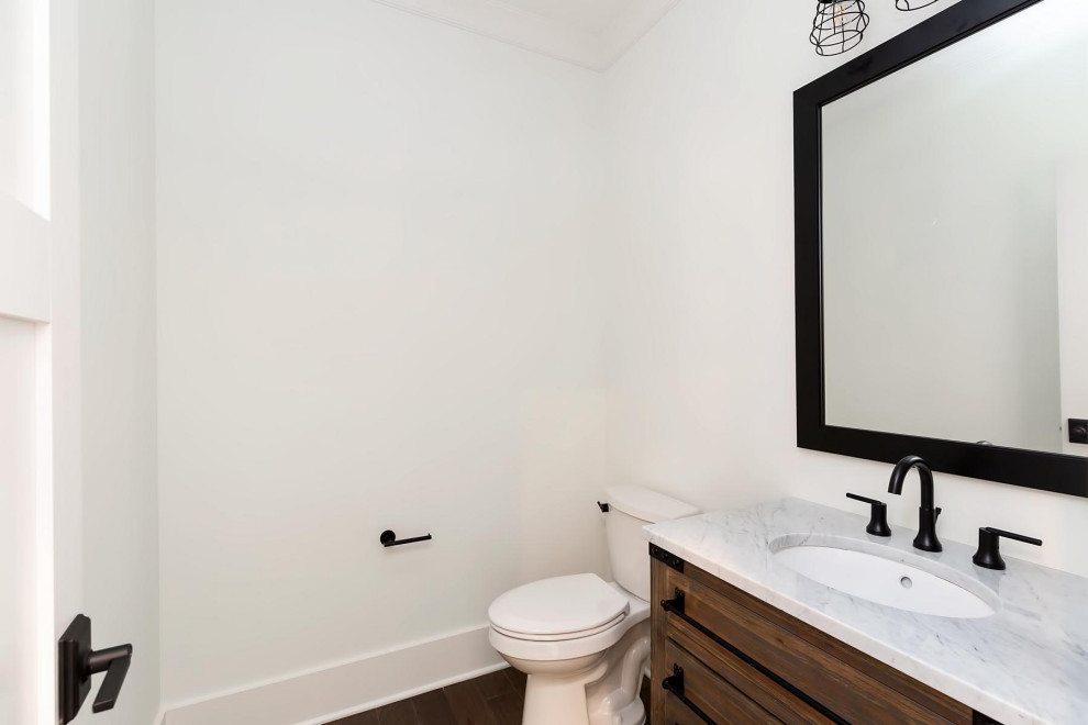This is an example of a mid-sized traditional powder room in Raleigh with furniture-like cabinets, medium wood cabinets, a two-piece toilet, grey walls, medium hardwood floors, an undermount sink, engineered quartz benchtops, brown floor and multi-coloured benchtops.