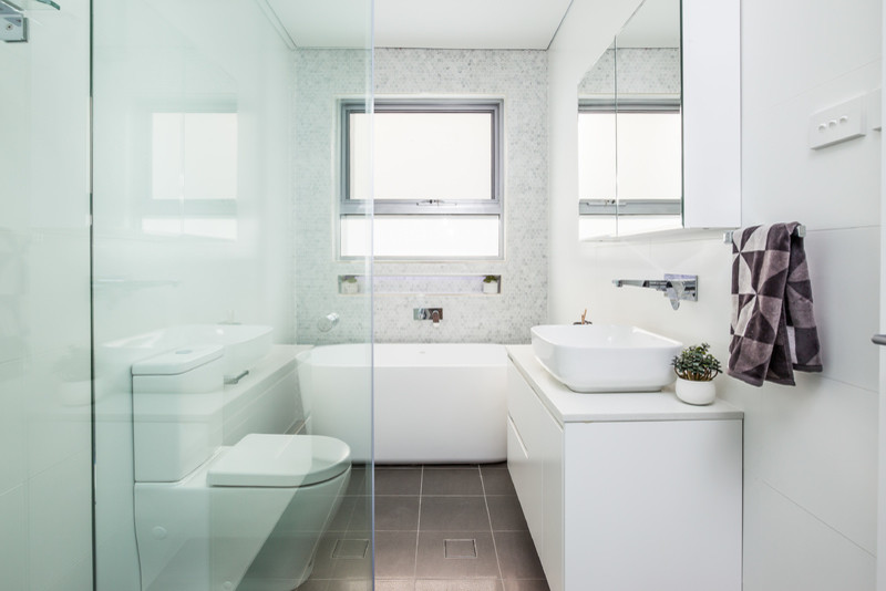 Design ideas for a small modern master bathroom in Sydney with gray tile, porcelain tile, porcelain floors, glass-front cabinets, white cabinets, a freestanding tub, a corner shower, a two-piece toilet, white walls, a console sink and granite benchtops.