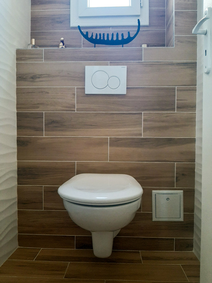Modern inredning av ett litet toalett, med en vägghängd toalettstol, brun kakel, vita väggar och brunt golv